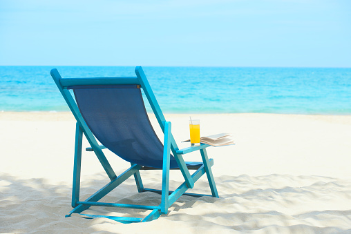 Chair with a glass of juice and book on sunny beach, tropical beach vacation and travel concept