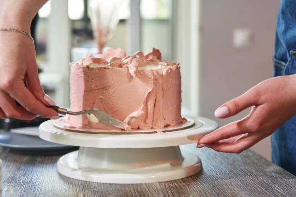 istock female hands level pink cream on a cake on a stand 1413977237