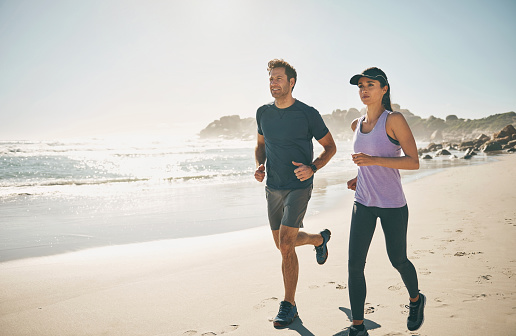 Fitness, active and sporty couple running and jogging together at the beach during sunset. Fit, energetic and healthy man and woman doing cardio exercise along a sandy shore with an ocean view