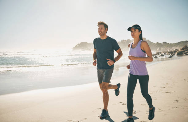 Fitness, active and sporty couple running and jogging together at the beach during sunset. Fit, energetic and healthy man and woman doing cardio exercise along a sandy shore with an ocean view stock photo