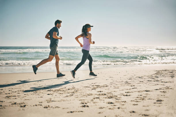 istock Fit, active and running couple on beach for workout, training and exercise by sea or ocean with copy space. Sporty, athletic and healthy man and woman jogging for cardio health, stamina and endurance 1413980849