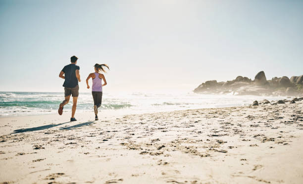 istock Couple jogging or doing endurance run on a beach together during summer with stunning ocean and nature background with copy space. Fit man and woman exercising for cardio stamina outdoors 1413980911