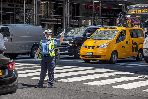 Midtown Manhattan, New York, NY, USA - July 1, 2022: Female African-American police officer regulating the traffic in the cross between 7th Avenue and West 34th Street