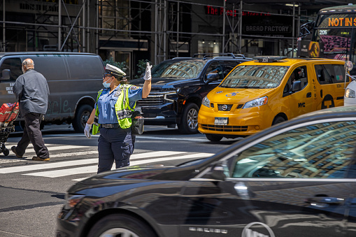 Midtown Manhattan, New York, NY, USA - July 1, 2022: Female African-American police officer regulating the traffic in the cross between 7th Avenue and West 34th Street