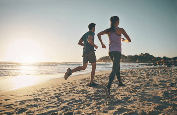 istock Active, athletic couple keeping fit running on ocean beach front for a healthy lifestyle. Joggers training, doing endurance morning workout. Back view of sporty pair doing cardio along the seaside. 1413983062