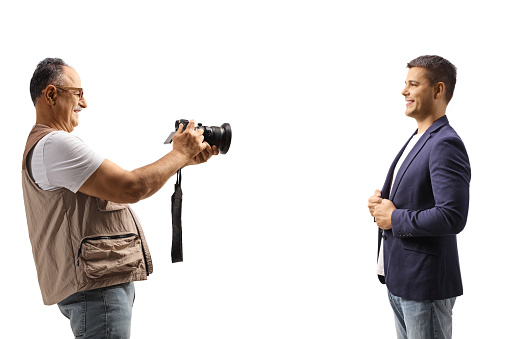 Mature man taking a photo of a young man with a professional camera isolated on white background