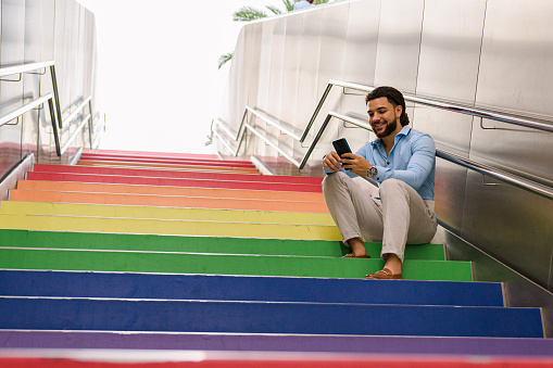 Latin man with dreadlocks sitting on a colorful staircase with his mobile phone