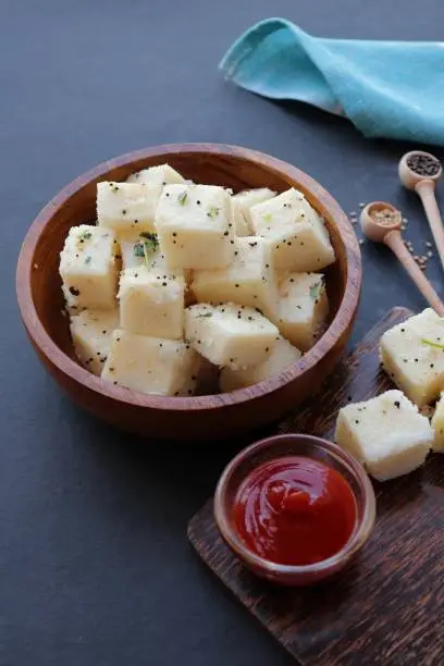 Photo of Indian popular Gujrati breakfast dish White Dhokla, Khatta Dhokla, Rice and Urad Dal Khaman. Also known as Instant Rava Dhokla. served with ketchup over black background. copy space.