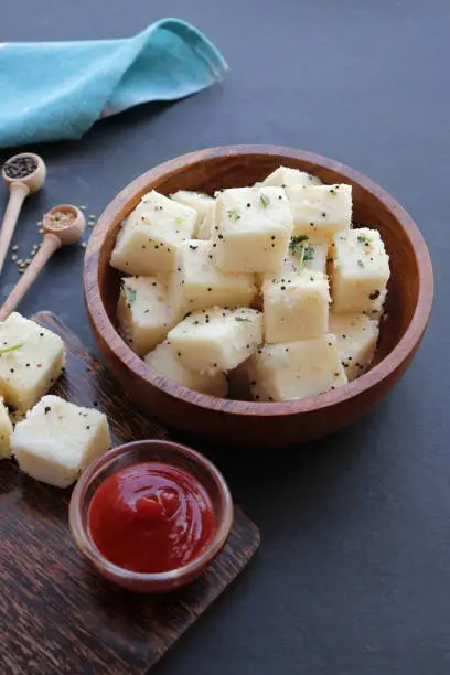 Photo of Indian popular Gujrati breakfast dish White Dhokla, Khatta Dhokla, Rice and Urad Dal Khaman. Also known as Instant Rava Dhokla. served with ketchup over black background. copy space.