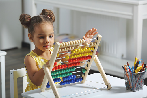 A Black girl is ready for a math and arithmetic lesson with an abacus. A pupil girl in a yellow dress counts an example in her mind. Math lesson in elementary school