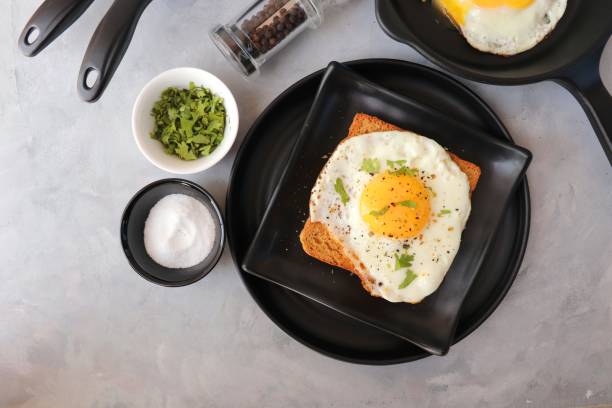 istock Fried Egg on Whole wheat Toast with salt and pepper for classic Breakfast. sunny side up egg with brown bread on black plate over wooden table, top view, copy space. 1413988186