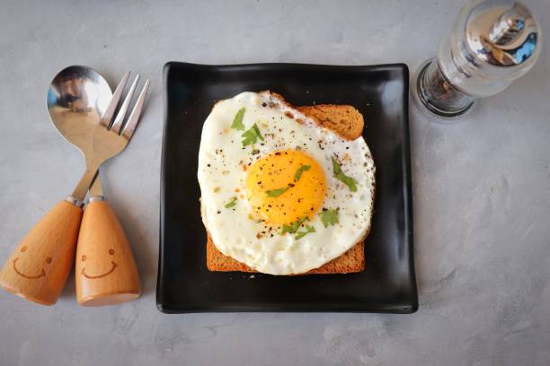 istock Fried Egg on Whole wheat Toast with salt and pepper for classic Breakfast. sunny side up egg with brown bread on black plate over wooden table, top view, copy space. 1413988764