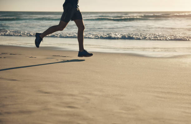 istock Active, fit and athletic man running on the beach for his morning exercise routine. Legs of a male athlete jogging and training cardio and fitness outdoors on the sea or ocean sand 1413988890
