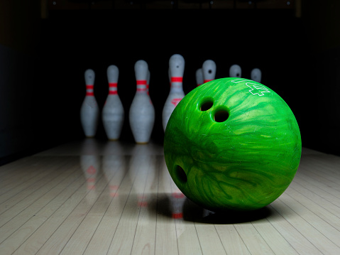 Green bowling ball and white skittles stand on a wooden bowling alley