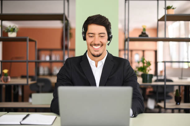 istock Young confident male remote consultant wearing headset using laptop computer to virtual connection 1413989748