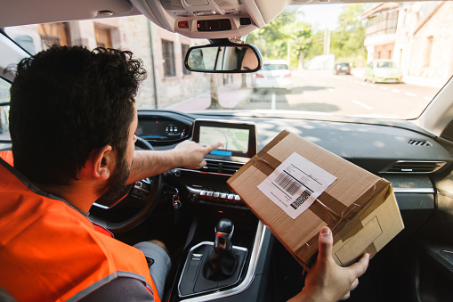 A young postal worker man entering an address from a package that he is holding in a GPS system
