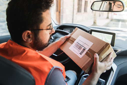 A delivery man inside his work car checking a package address tag before delivering it