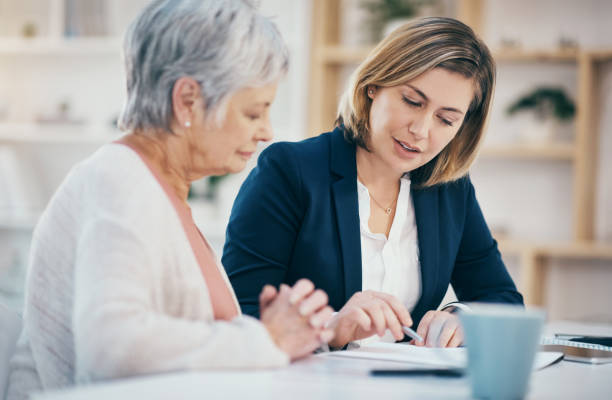Talking financial advisor helping senior with paperwork, retirement budget and managing pension fund. Finance worker explaining and showing old woman where to sign will agreement and banking contract stock photo