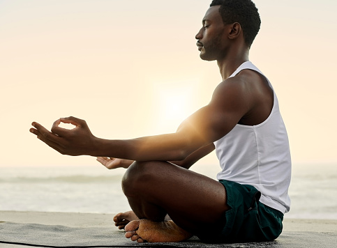 Spiritual, calm and relaxed man doing lotus yoga pose exercise and mediation with sunset beach background and copy space. Young athletic, fit and healthy yogi guy practicing inner peace by the ocean