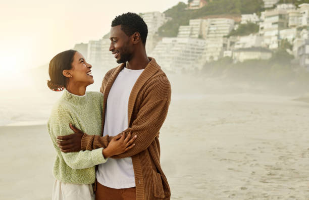 istock Laughing, hugging and in love couple on beach bonding, embracing and enjoying relaxing sunset date together by sea or ocean. Smiling, romantic and loving man and woman holding each other on holiday 1413996708