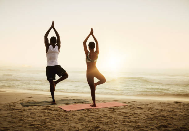 Fit, active and healthy beach yoga people holding tree pose while stretching, balancing or exercising for pilates or meditation by sea or ocean. Calm, serene or zen yogis in holistic sunrise exercise