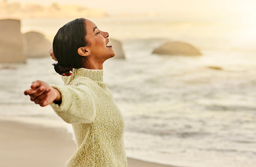 Carefree,calm and happy of a woman at the beach at sunset. Female stretching her arms on a seaside feeling free and relaxed, enjoying a golden twilight outside in nature on a peaceful vacation