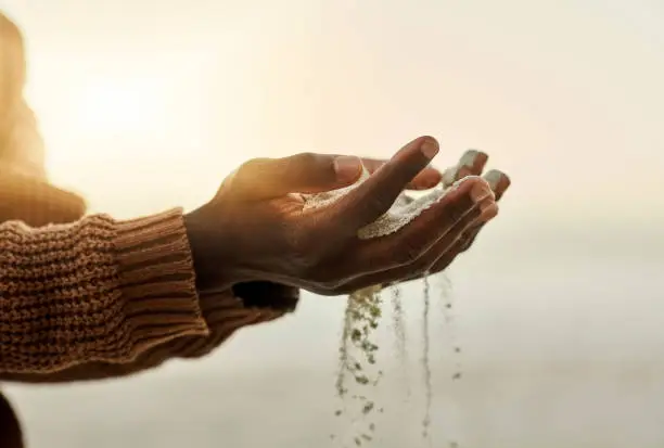 Photo of Closeup pouring sand through hands on the beach during sunset. Man holding or playing with soft soil grains while it runs through fingers outside in nature near the ocean in summer with copy space