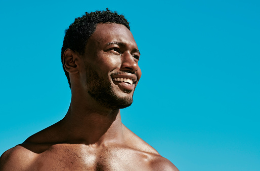 Handsome, happy and confident black man posing against a perfect and clear blue sky copy space background. Beauty closeup of the face and head of a young african american male outside from below