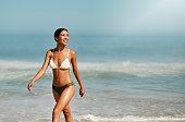 istock Fit, beautiful and toned bikini model on beach enjoying fun and relaxing summer holiday by ocean and sea while wearing a swimsuit. Smiling, happy and walking woman in swimwear on a tropical vacation 1413996841