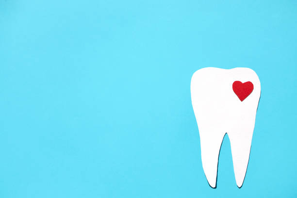 istock Silhouette of a tooth with a red heart on a blue background. Flat lay, place for text. 1413998043