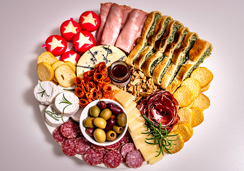 Top view of lunch meal or appetiser including a single dish with salami, pepperoni, brie cheese, ham. Aerial view of one plate with dinner or appetiser composed by cured meat, cheeses, nuts and bread
