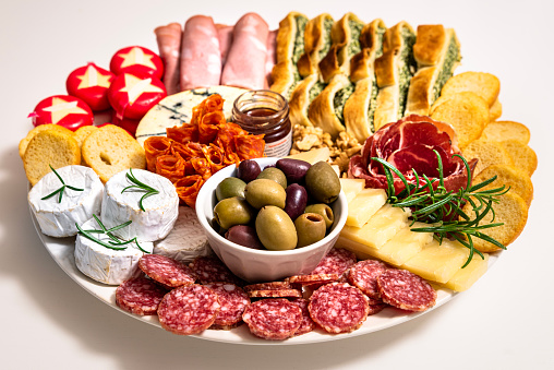 Lunch meal or appetiser including a single dish with salami, pepperoni, brie cheese, ham. One plate with dinner or appetizer consisting of salumi (cured meat), cheeses, nuts and focaccia bread