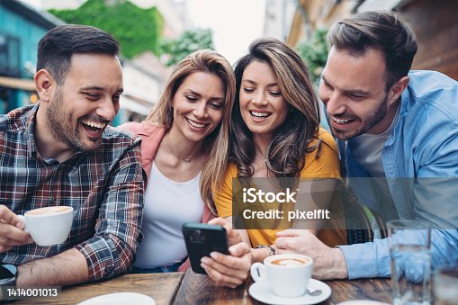 istock Group of friends sitting in cafe and looking at smart phone 1414001013