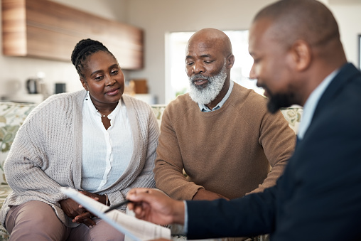 Mature black couple discussing their finances and planning retirement with an advisor at home. Senior husband and wife getting help with paperwork, investments or savings by a trusted agent