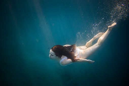 Women with long brown hair and white swimsuit diving underwater
