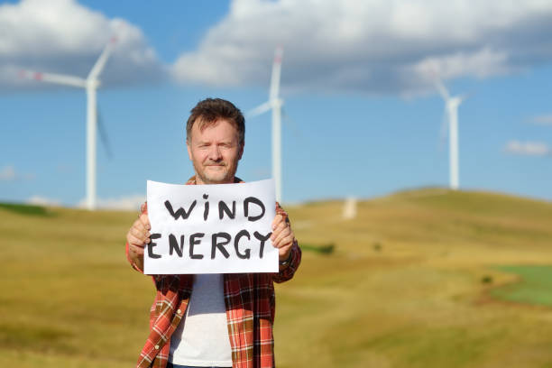 ativista ecológico com bandeira energia eólica no fundo de usinas para produção de energia elétrica renovável. pessoa e moinhos de vento. turbinas eólicas altas para geração de eletricidade. energia verde - 13589 - fotografias e filmes do acervo