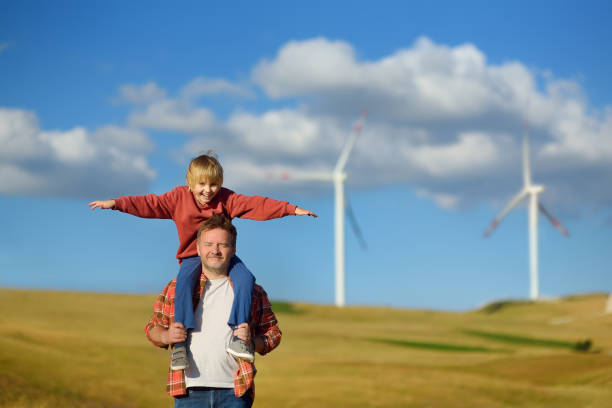 ativistas ecológicos homem e criança no fundo de usinas para produção de energia elétrica renovável. pessoas e moinhos de vento. turbinas eólicas altas para geração de eletricidade. energia verde - 13601 - fotografias e filmes do acervo