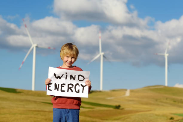 eco activist boy with banner "wind energy" on background of power stations for renewable electric energy production. child and windmills. high wind turbines for generation electricity. green energy - 13603 imagens e fotografias de stock