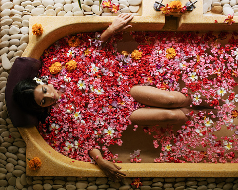 Overhead shot of woman relaxing in bathtub with flower petals. Female taking flower bath at spa center.