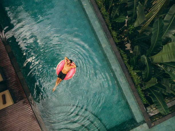 jovem relaxando em anel inflável na piscina do resort - floating on water swimming pool men water - fotografias e filmes do acervo