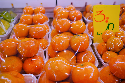Fresh oranges at market stall display wrapped in plastic film wrap for protection of the fruits. The plastic wrappers are wasteful and unsustainable for the environment