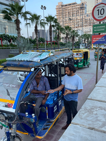 Delhi, India - August 9, 2022: Stock photo showing parked auto rickshaw driver being paid by passenger at end of a ride.