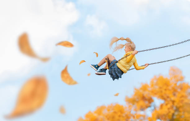 uma criança feliz cavalga em um balanço no outono. - andar de balanço - fotografias e filmes do acervo