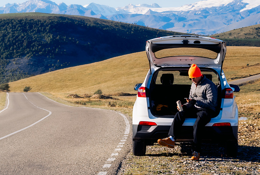 tourist rest - a man sits in the trunk of his car on the side of the road in the mountains, a beautiful landscape