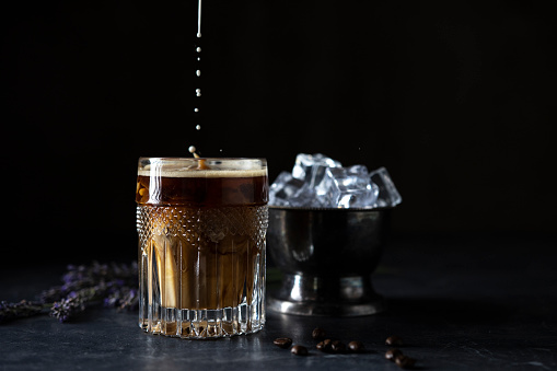 Iced coffee with milk in glass on dark background.