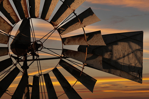 The sun sets behind an antique windmill in a composite image.