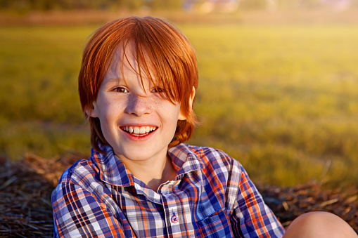 Happy smiling boy with red hair and freckles in the field, portrait of about 8 years old, summer time
