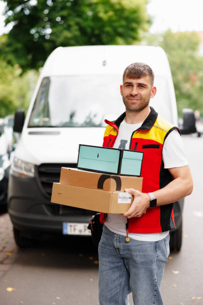 istock Man standing in front of a minibus working for a delivery service holding packages to be delivered 1414015708
