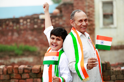 Grandfather and grandchild holding national flag in hands during Independence day/ Republic day at home portrait close up.