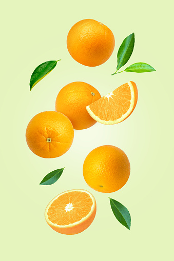 Orange fruit with cut half slice and green leaf flying in the air isolated on green color background.